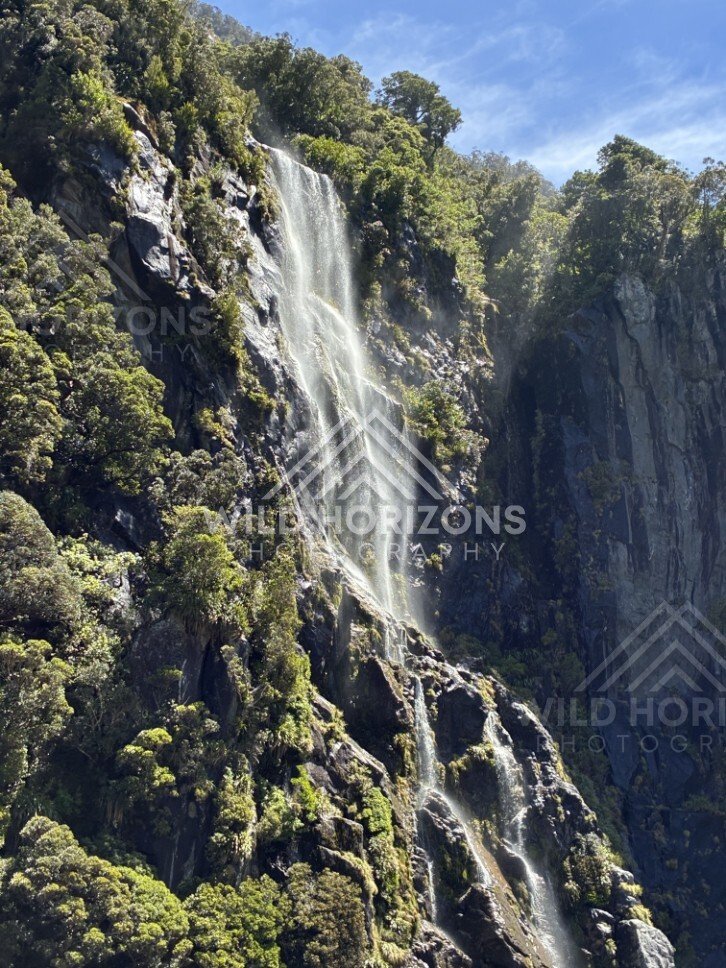Sunlit Waterfall Cascading Over Dark Rock Ledges. Milford Sound, New Zealand.