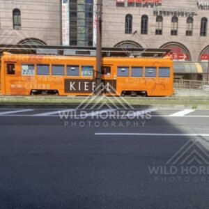 Orange Streetcar Passing Through a Sunlit Osaka Street. Osaka, Japan.