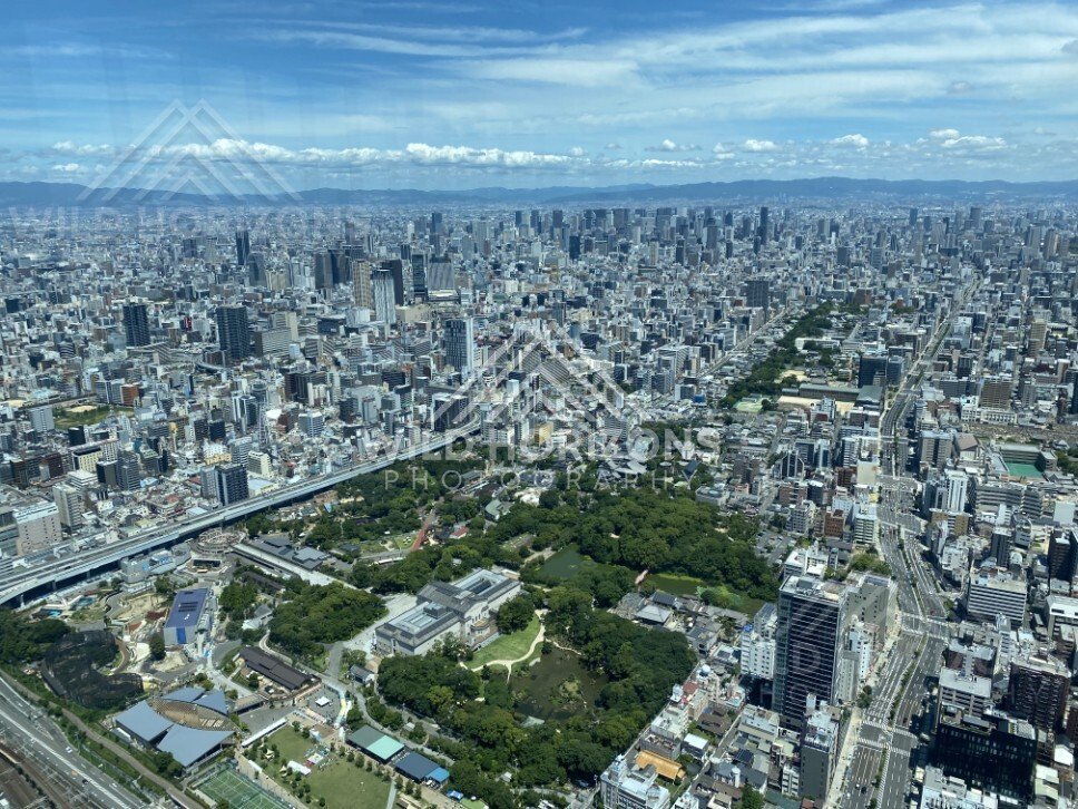 Osaka Skyline Above a Green Urban Park Under Layered Summer Clouds. Umeda Sky Building, Osaka, Japan.