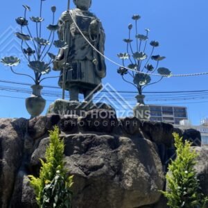 Buddhist Statue on Stone Plinth with Lotus Lanterns Against Blue Sky. Shitennoji Temple, Osaka, Japan.