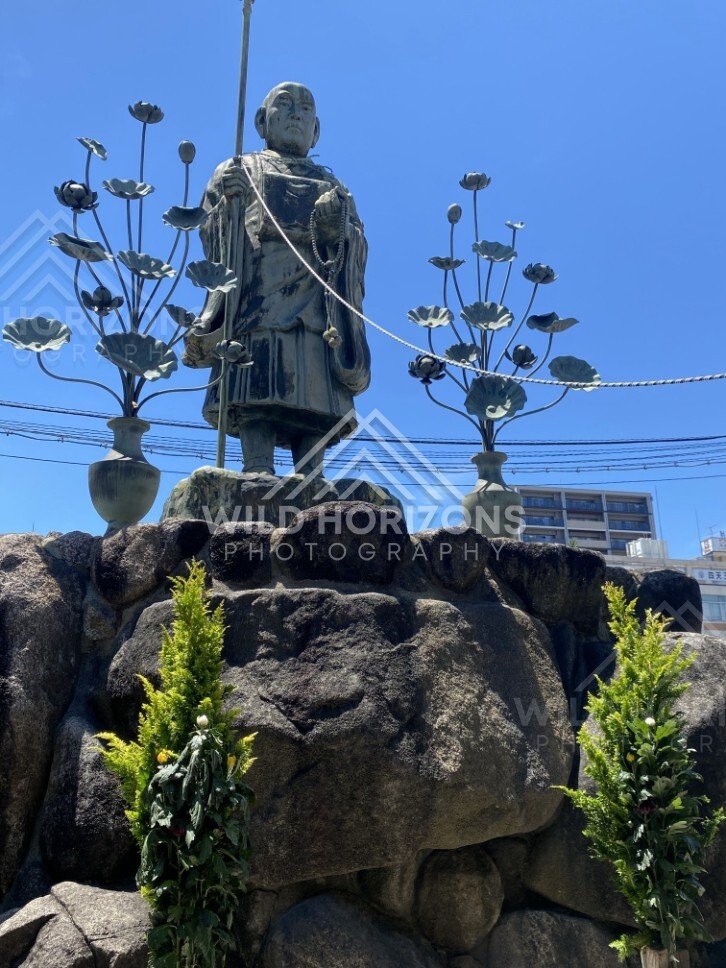 Buddhist Statue on Stone Plinth with Lotus Lanterns Against Blue Sky. Shitennoji Temple, Osaka, Japan.