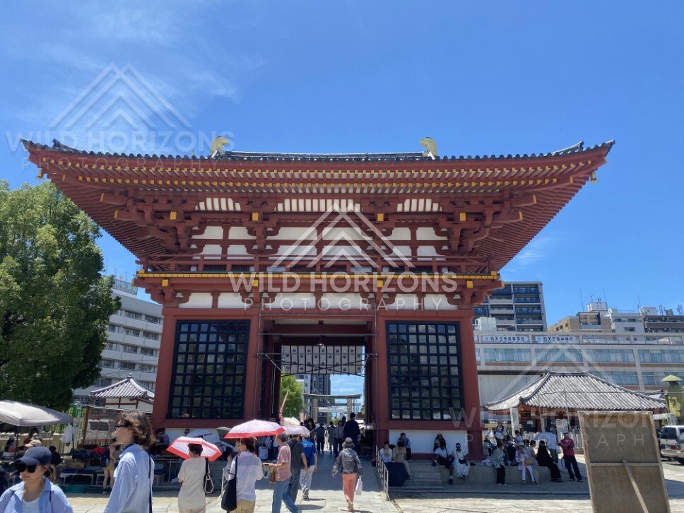 Grand Temple Gate Framed by City Buildings and a Busy Courtyard. Shitennoji Temple, Osaka, Japan.