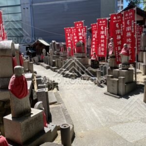 Jizo statues and memorial stones beneath red banners at Shitennoji. Shitennoji Temple, Osaka, Japan.