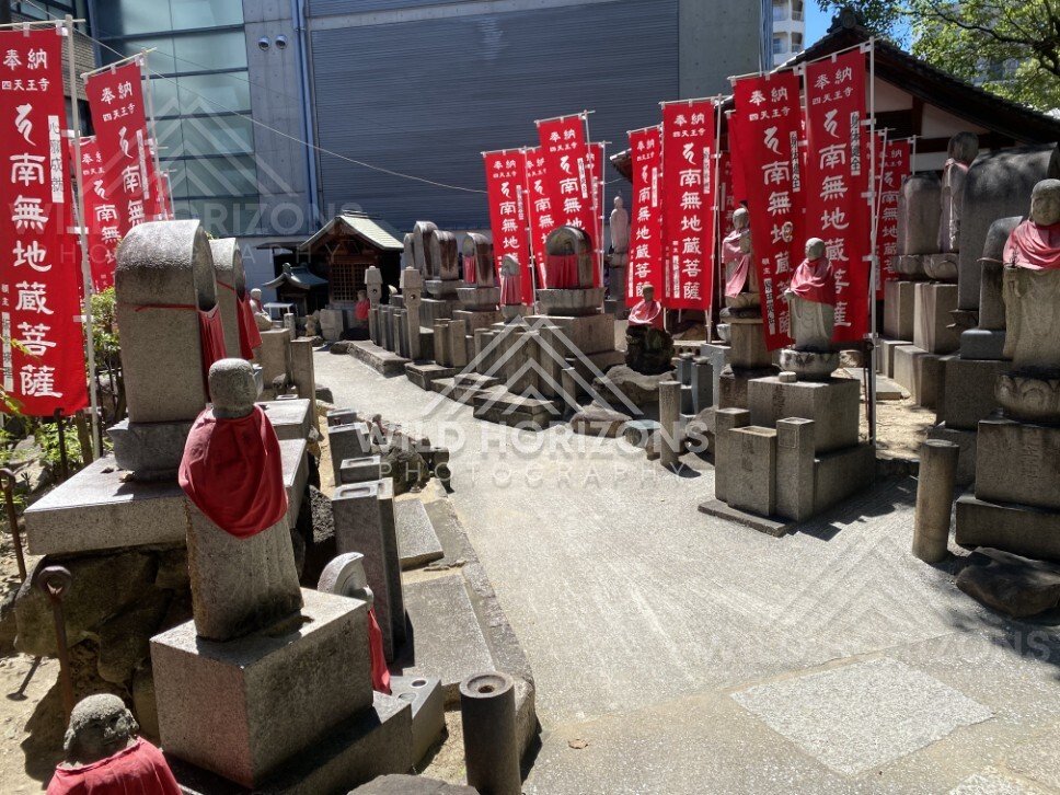 Jizo statues and memorial stones beneath red banners at Shitennoji. Shitennoji Temple, Osaka, Japan.
