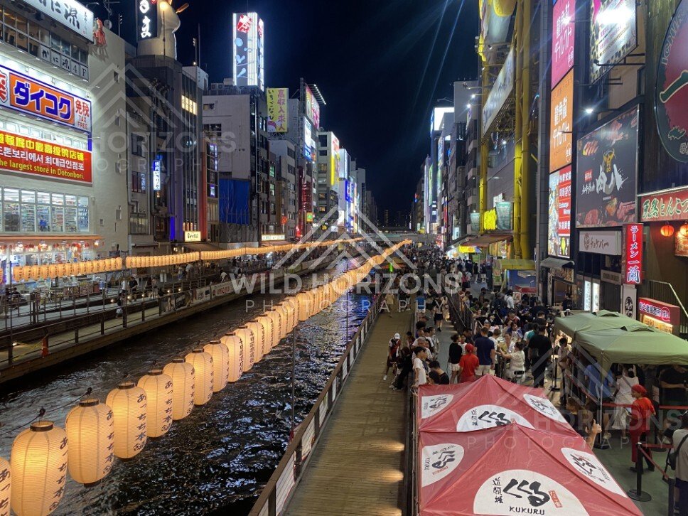 Crowds and lantern reflections along the Dotonbori canal at night. Dotonbori, Osaka, Japan.