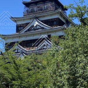 Hiroshima Castle keep rising above green trees on a clear day. Hiroshima Castle, Hiroshima, Japan.