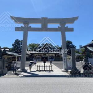 Large stone torii framing a shrine approach with visitors walking through. Hiroshima, Japan.