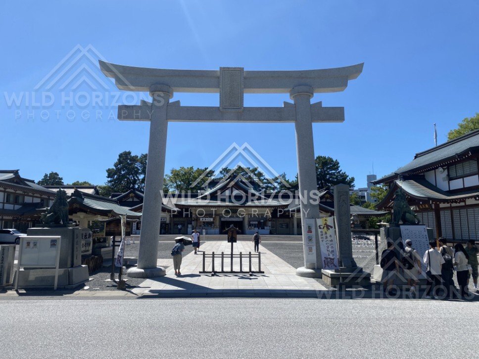 Large stone torii framing a shrine approach with visitors walking through. Hiroshima, Japan.