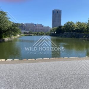 Broad moat and skyline view with a tall tower beyond the trees. Hiroshima, Japan.