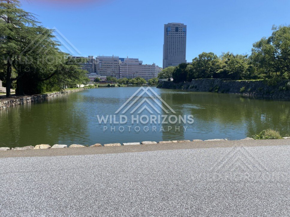 Broad moat and skyline view with a tall tower beyond the trees. Hiroshima, Japan.