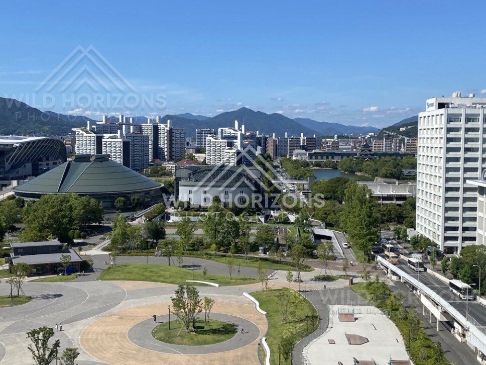 Wide city panorama with distinctive civic buildings and open plazas below. Hiroshima, Japan.