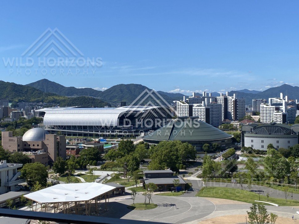 Stadium and civic buildings set against forested hills beyond the city. Hiroshima, Japan.