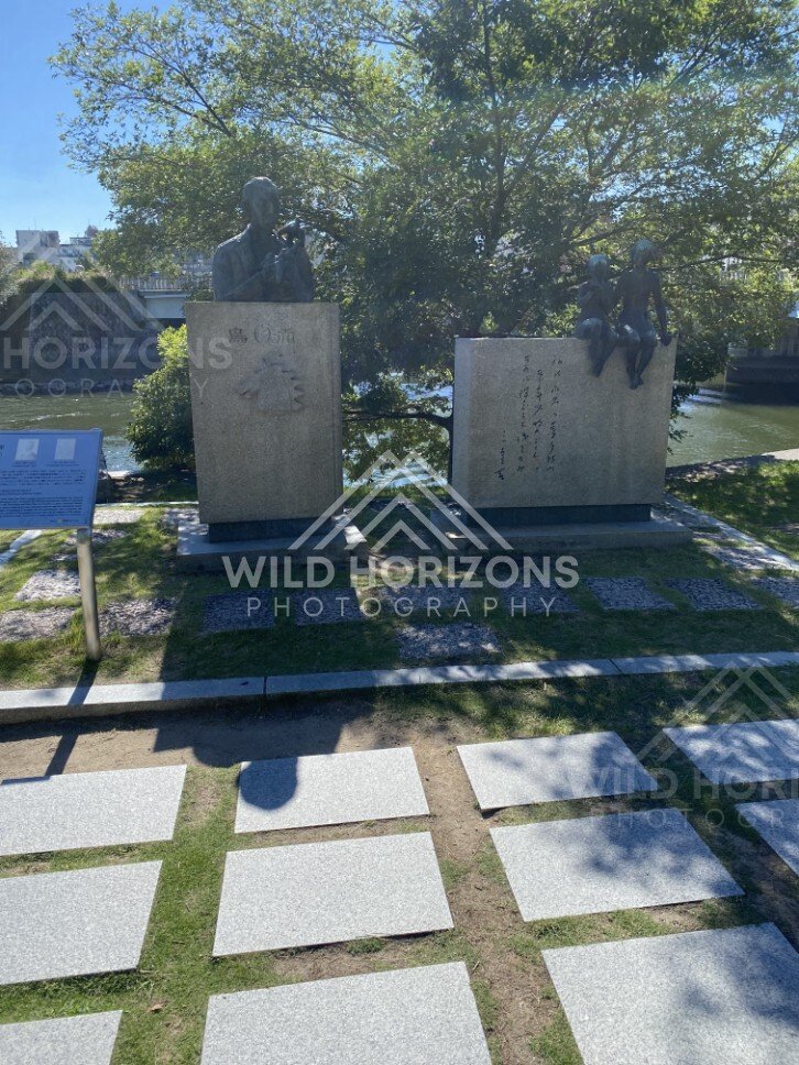 Bronze statues and engraved stone blocks beside a riverside path. Hiroshima Peace Memorial Park, Hiroshima, Japan.
