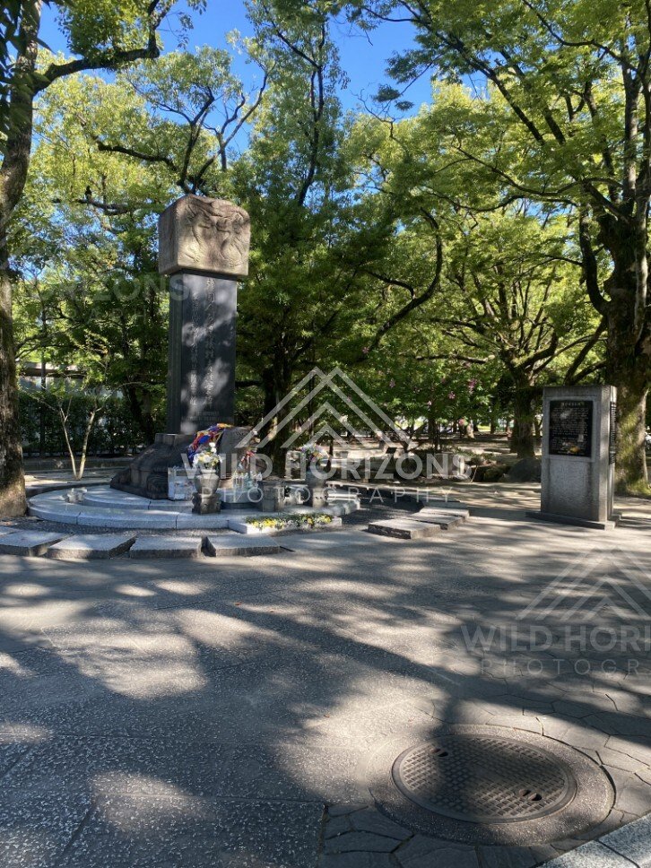 Memorial mound and monument set within tree-filled Peace Memorial Park. Hiroshima Peace Memorial Park, Hiroshima, Japan.