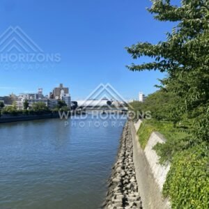 River channel bordered by stone embankments under clear blue skies. Hiroshima, Japan.