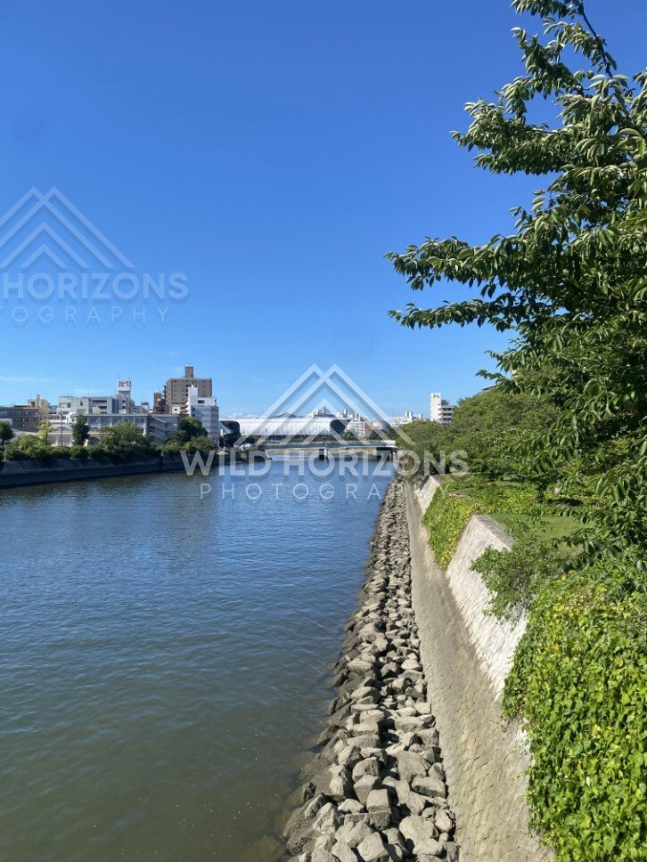 River channel bordered by stone embankments under clear blue skies. Hiroshima, Japan.