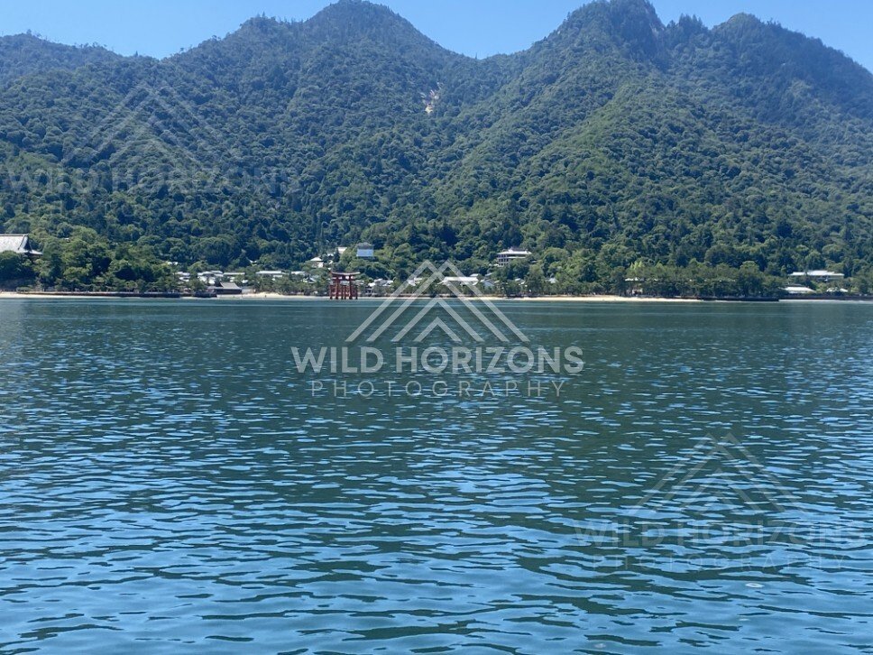 Distant torii gate visible across the water from the shoreline. Miyajima, Hiroshima, Japan.