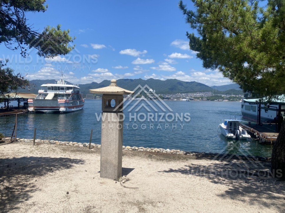 Stone lantern and boats beside the waterfront with mountains beyond. Miyajima, Hiroshima, Japan.