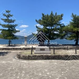 Statue facing the sea along a paved waterfront promenade. Miyajima, Hiroshima, Japan.