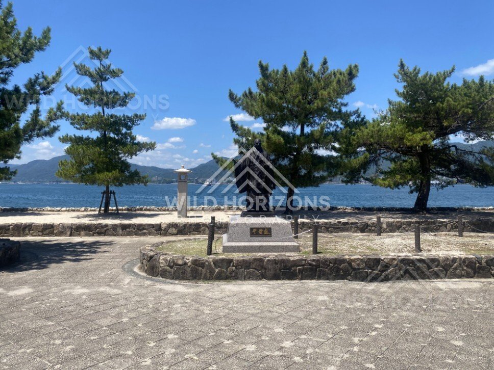 Statue facing the sea along a paved waterfront promenade. Miyajima, Hiroshima, Japan.
