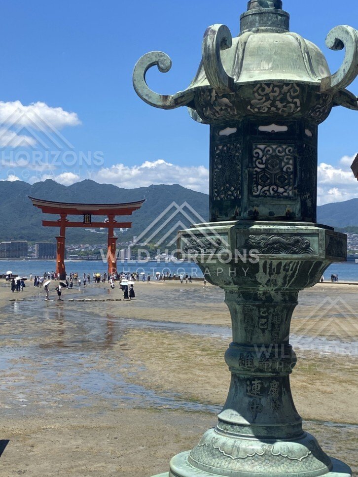 Close view of ornate bronze lantern with the torii gate beyond. Miyajima, Hiroshima, Japan.