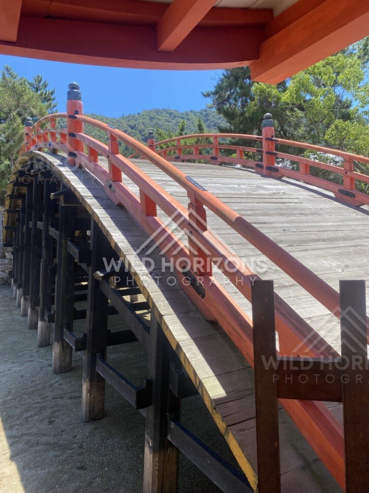 Red arched bridge rising above the shrine courtyard. Miyajima, Hiroshima, Japan.
