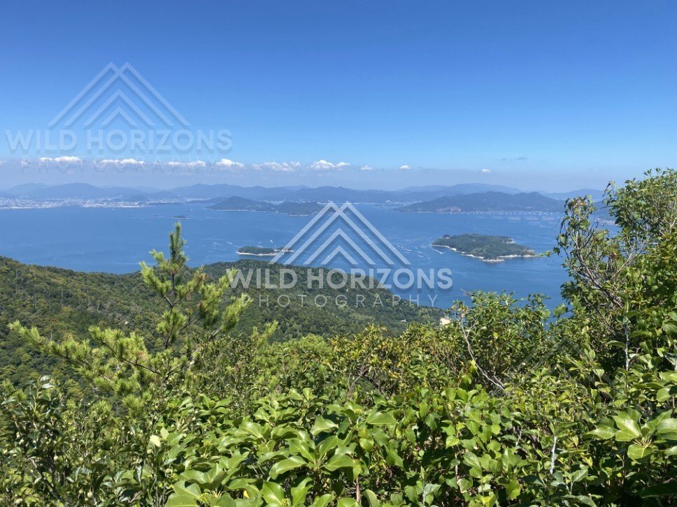 Wide coastal view across blue water toward distant mountains. Miyajima, Hiroshima, Japan.