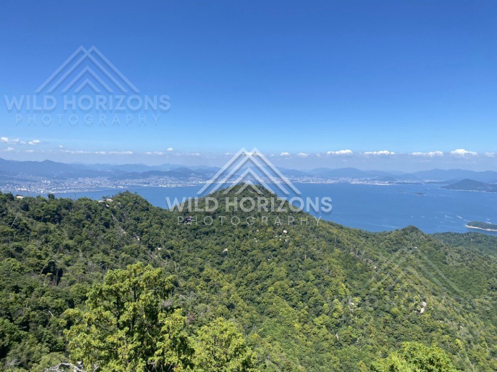 Panoramic view across forested ridges toward distant coastline. Miyajima, Hiroshima, Japan.