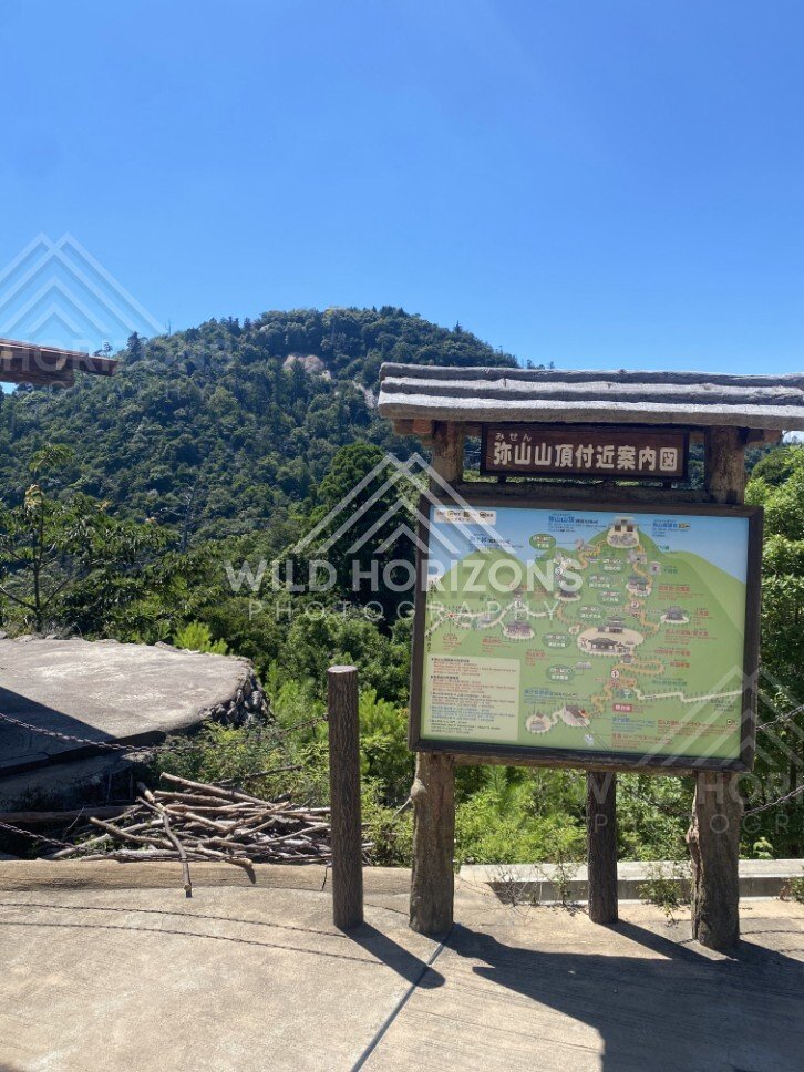 Trail map signboard at mountain lookout with hills beyond. Miyajima, Hiroshima, Japan.