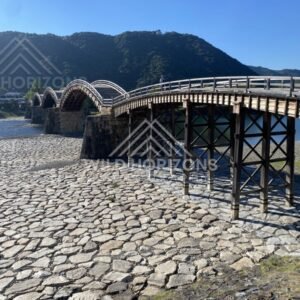 Kintaikyo Bridge seen from riverbank with arches reflected in calm water. Iwakuni, Yamaguchi, Japan.