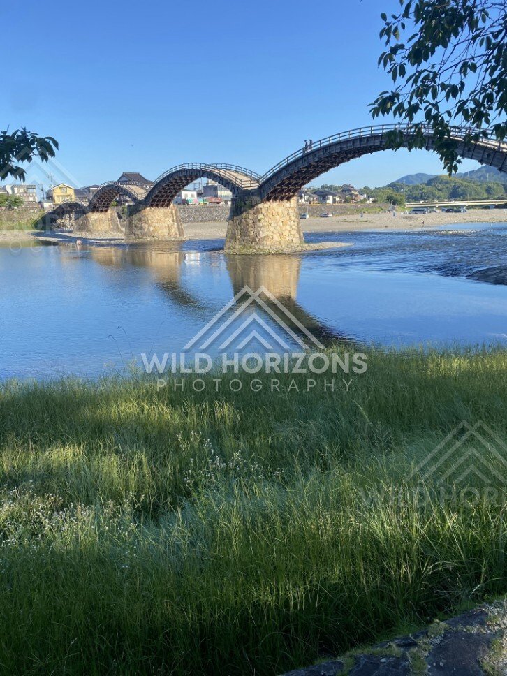 Kintaikyo Bridge crossing a shallow river under bright blue skies. Iwakuni, Yamaguchi, Japan.