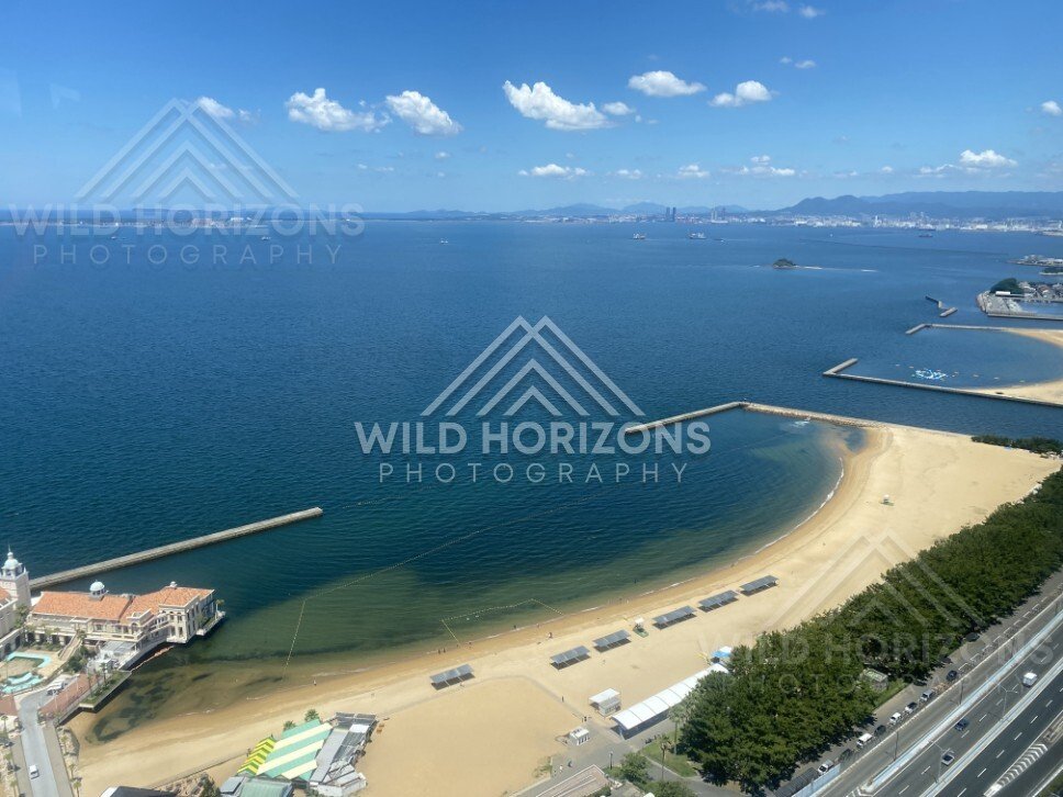 Wide coastal panorama with beach, sea, and distant city skyline. Fukuoka, Japan.