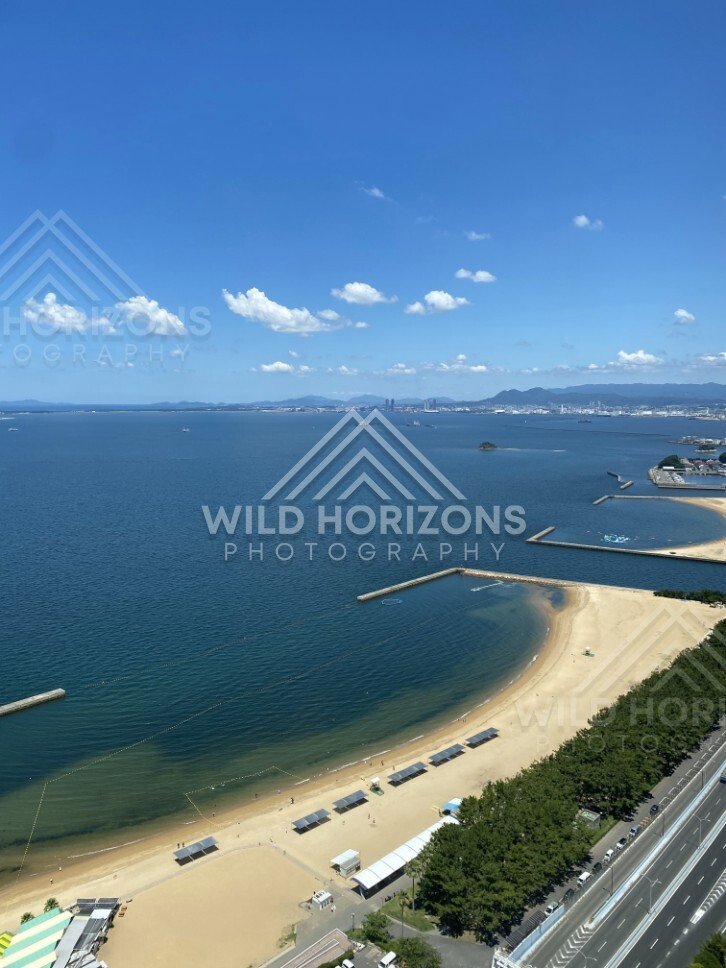 Elevated coastal view with beach, road, and offshore structures. Fukuoka, Japan.