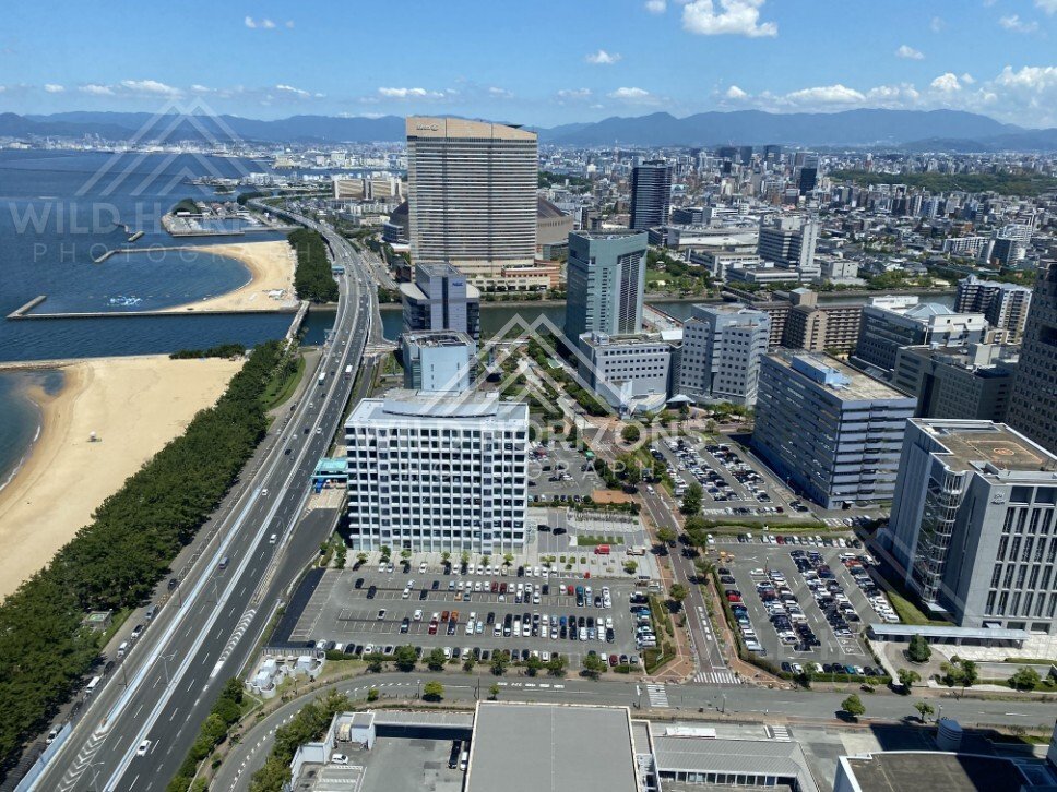 Urban coastline where highway, buildings, and beach meet the sea. Fukuoka, Japan.