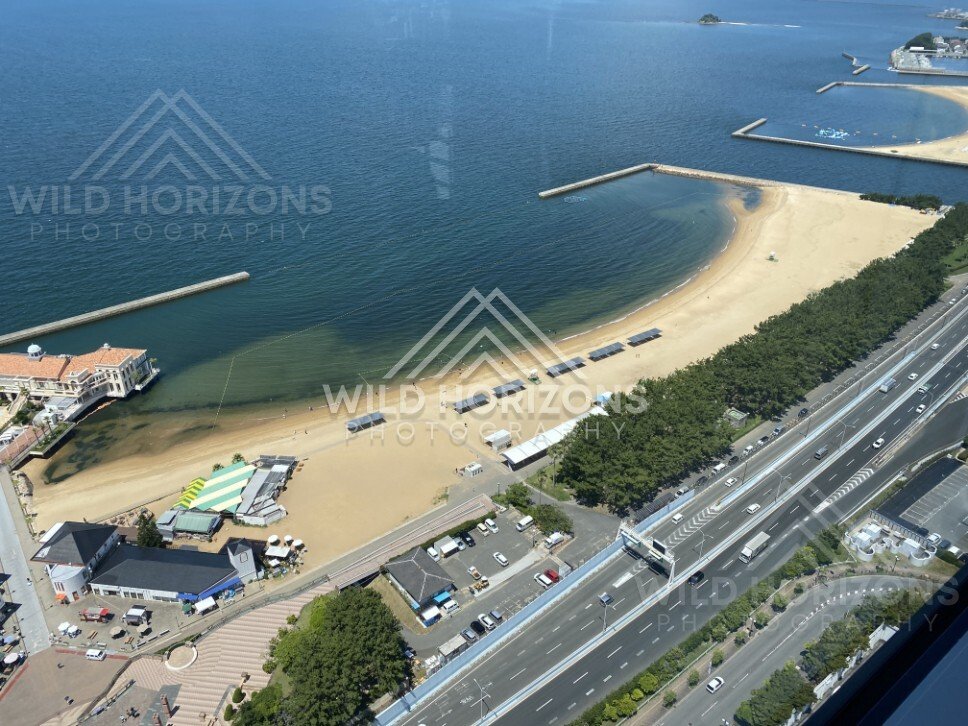 Aerial view of curved beach and marina structures along the coast. Fukuoka, Japan.
