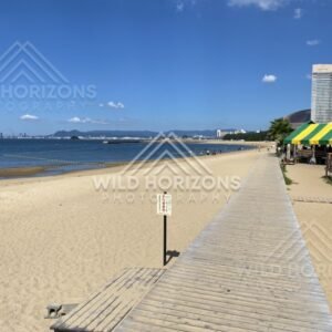 Boardwalk running parallel to sandy beach under clear blue sky. Fukuoka, Japan.