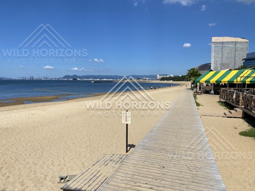 Boardwalk running parallel to sandy beach under clear blue sky. Fukuoka, Japan.