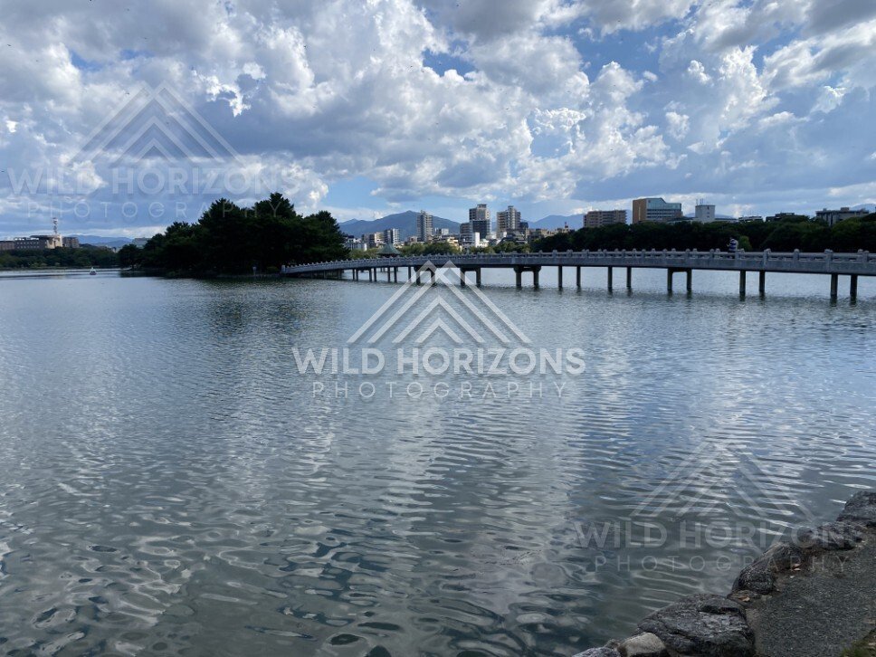 A long pedestrian bridge crosses the lake toward the city skyline. Fukuoka, Japan.