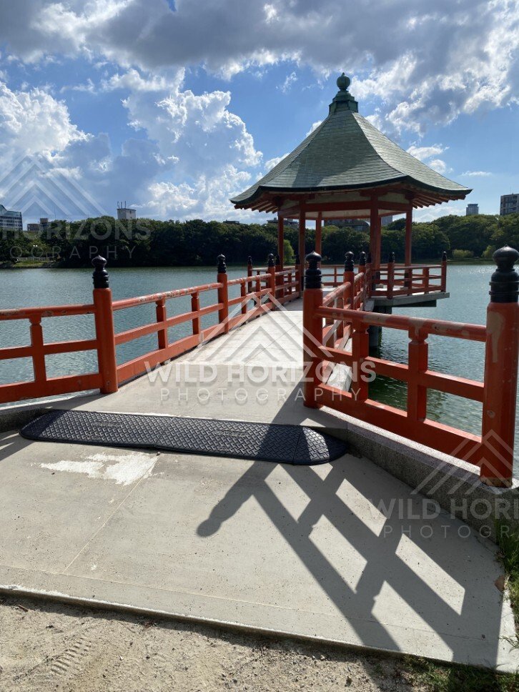 A red pavilion and walkway extend out over the lake under towering clouds. Fukuoka, Japan.