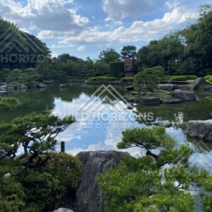 Clouds reflect in a still pond with boulders and clipped pines in the foreground. Fukuoka, Japan.