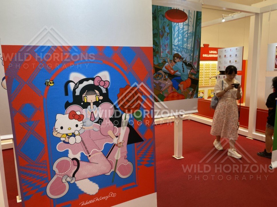 Visitors exploring a Hello Kitty pop culture exhibition with framed artworks. Fukuoka, Japan.