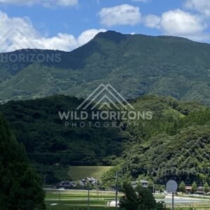 Green mountain ridge rising above rural fields and a small valley settlement. Nagasaki, Japan.