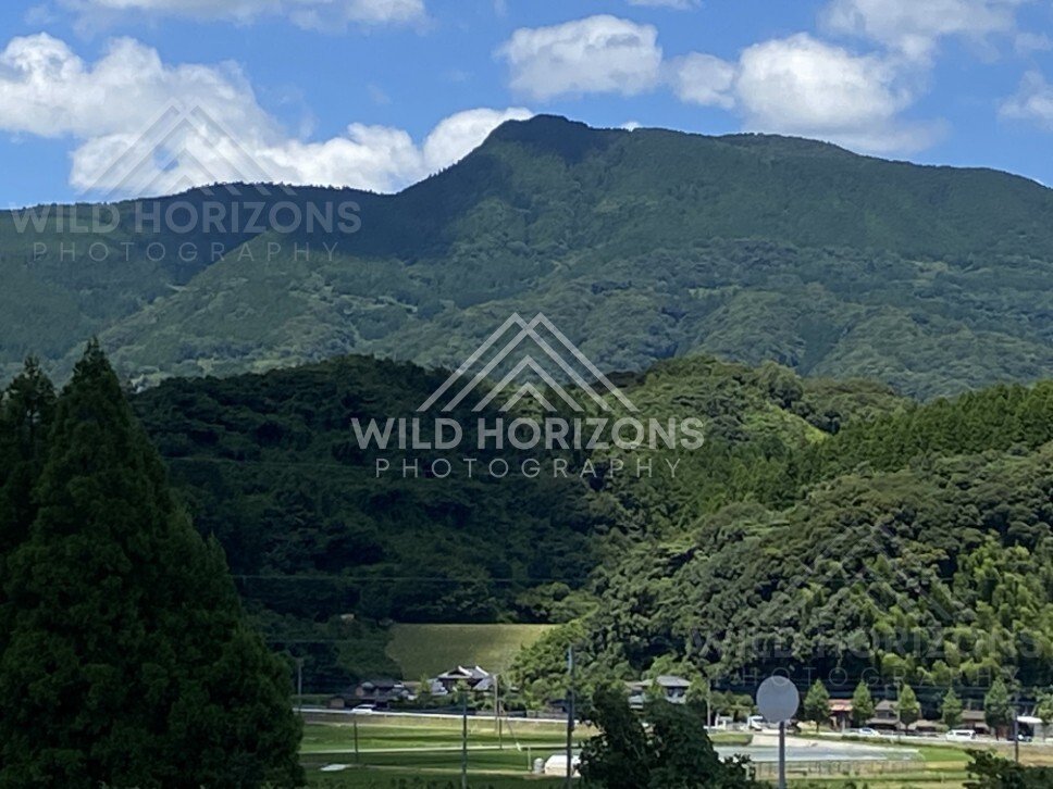Green mountain ridge rising above rural fields and a small valley settlement. Nagasaki, Japan.