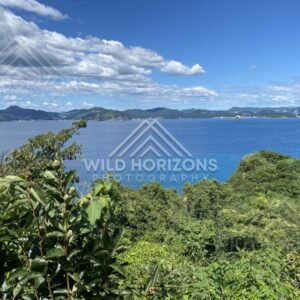 Blue bay and distant mountains beneath a sky filled with scattered white clouds. Nagasaki, Japan.