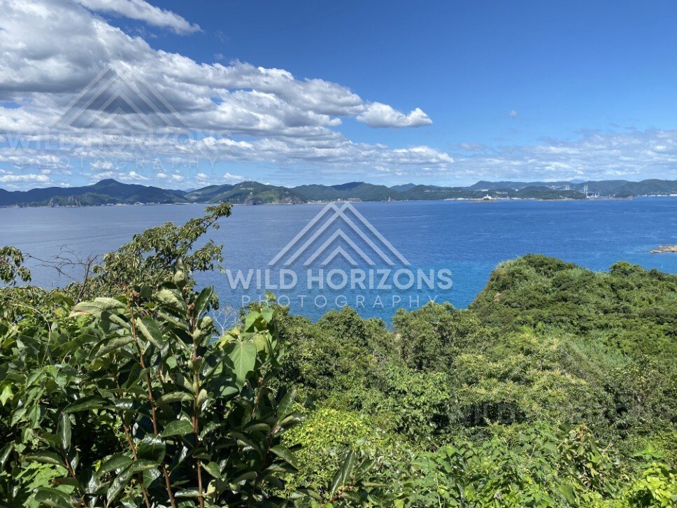 Blue bay and distant mountains beneath a sky filled with scattered white clouds. Nagasaki, Japan.