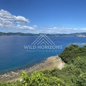 Coastal headland view with clear water, rocky shore, and distant mountains. Nagasaki, Japan.