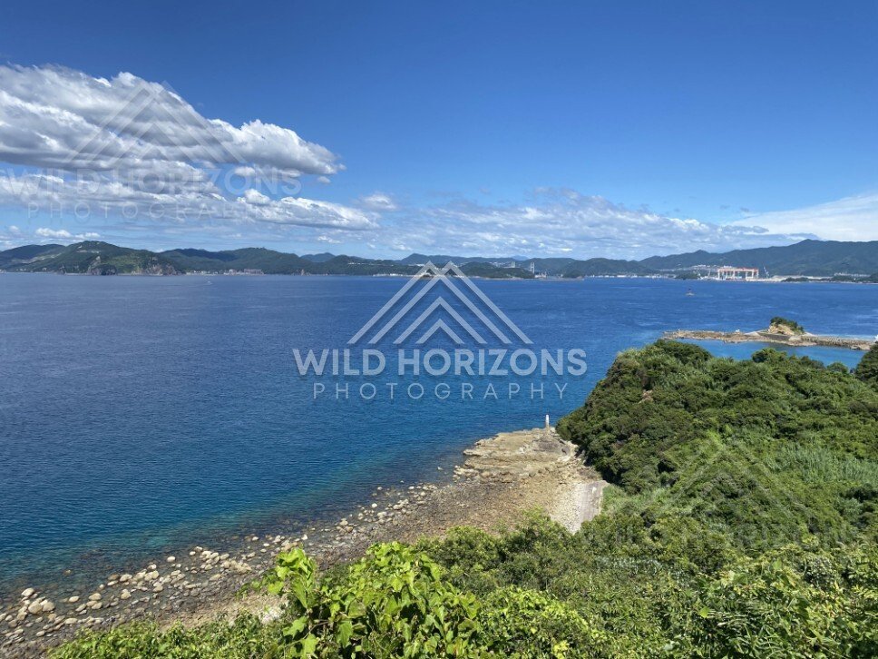 Coastal headland view with clear water, rocky shore, and distant mountains. Nagasaki, Japan.