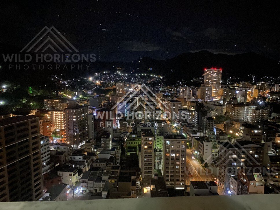 Night cityscape with glowing streets and mountains silhouetted beyond the skyline. Nagasaki, Japan.