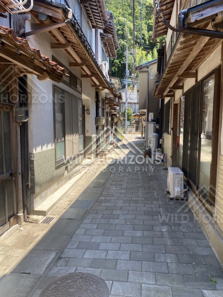 Narrow Paved Alley With Eaves, Wires, and Bamboo Hillside. Mihonoseki, Japan.