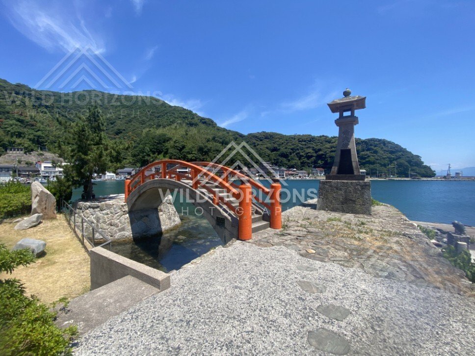 Red arched Bentenjima Bridge beside a stone lantern on the harbour. Mihonoseki, Japan.